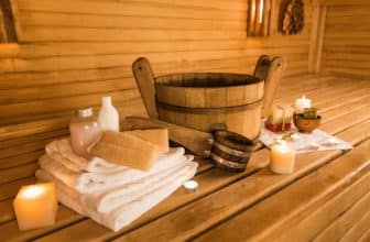 Ein Aufgusseimer, Handtücher, Kerzen und Schwämme auf der Bank einer Sauna.